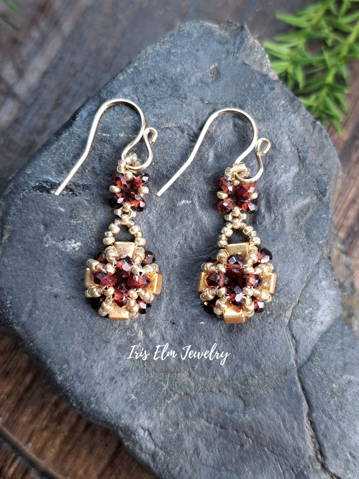 a pair of handmade red garnet gemstone and gold glass beaded earrings by Iris Elm Jewelry on rocky surface