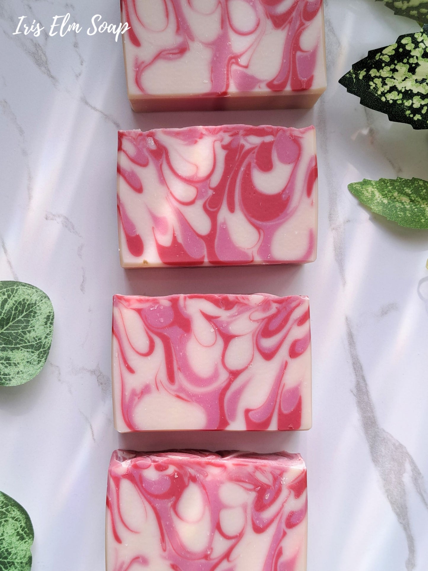 Marbled pink and white strawberry peach handmade soap bars on a marble surface with green leaves.