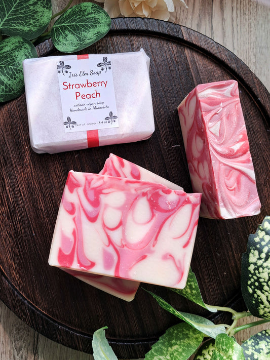 Three bars of strawberry peach soap on a wooden tray with greenery around.