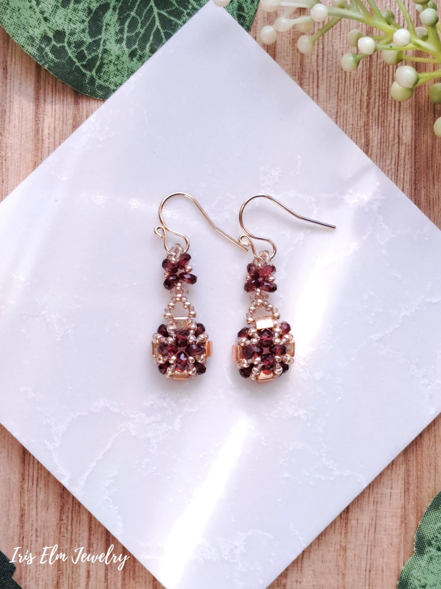Pair of faceted garnet and gold glass beadwork earrings with red gemstones on a white tile