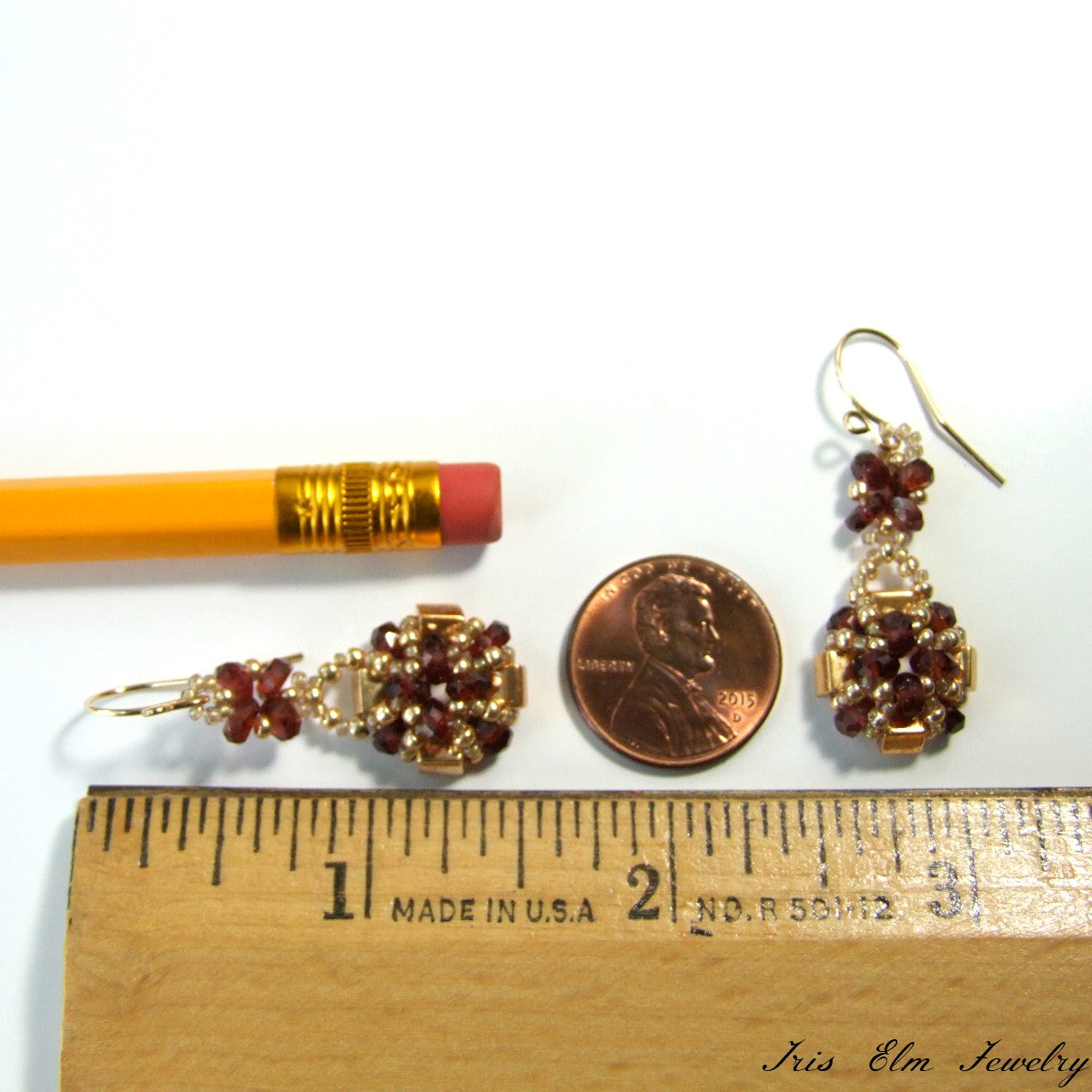 Pair of gold earrings with red faceted garnet gemstones next to a penny and ruler for scale on a white background