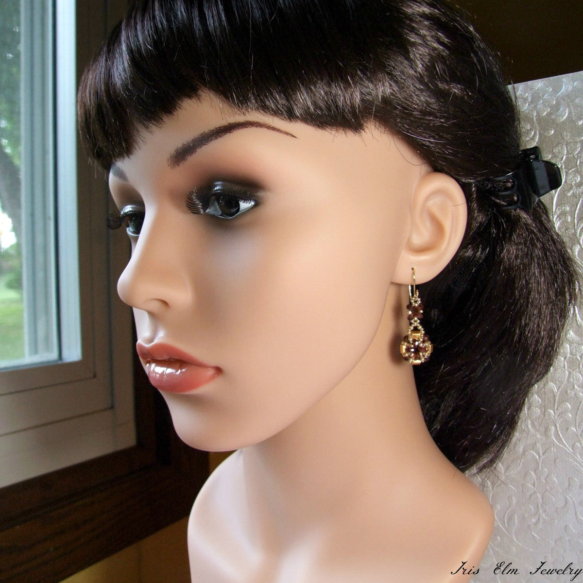 Mannequin head with a styled haircut and garnet and gold glass earrings in front of a window.