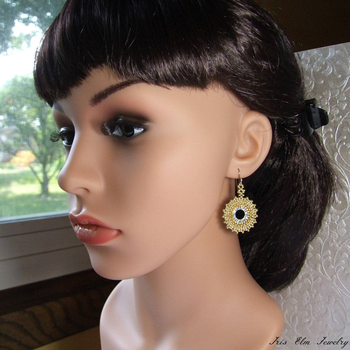 Mannequin head with dark hair and gold earrings, set against a neutral background.