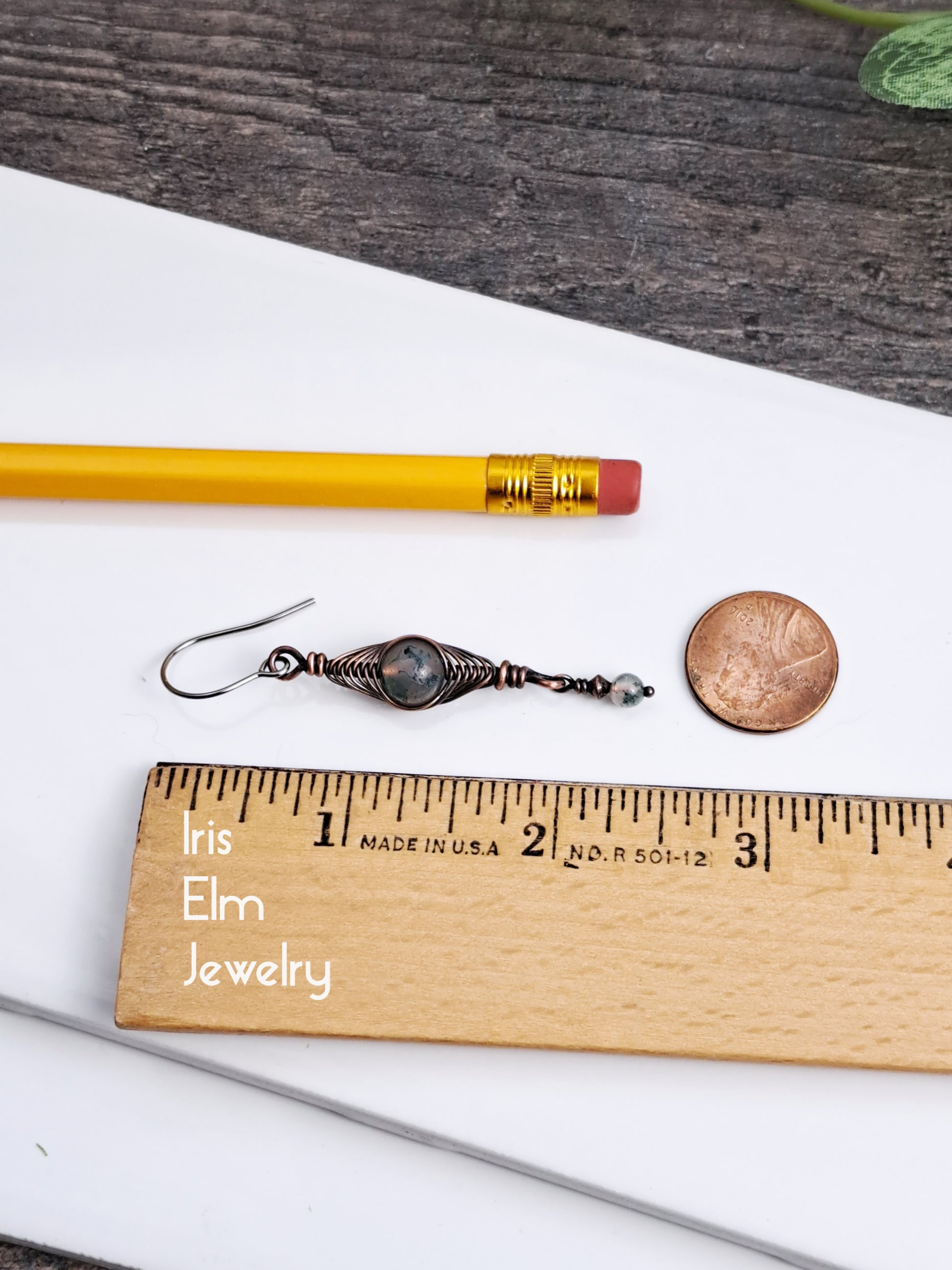 2 and 3/8 inch long moss agate Earrings next to a pencil and penny on a wooden ruler with 'Iris Elm Jewelry' branding.