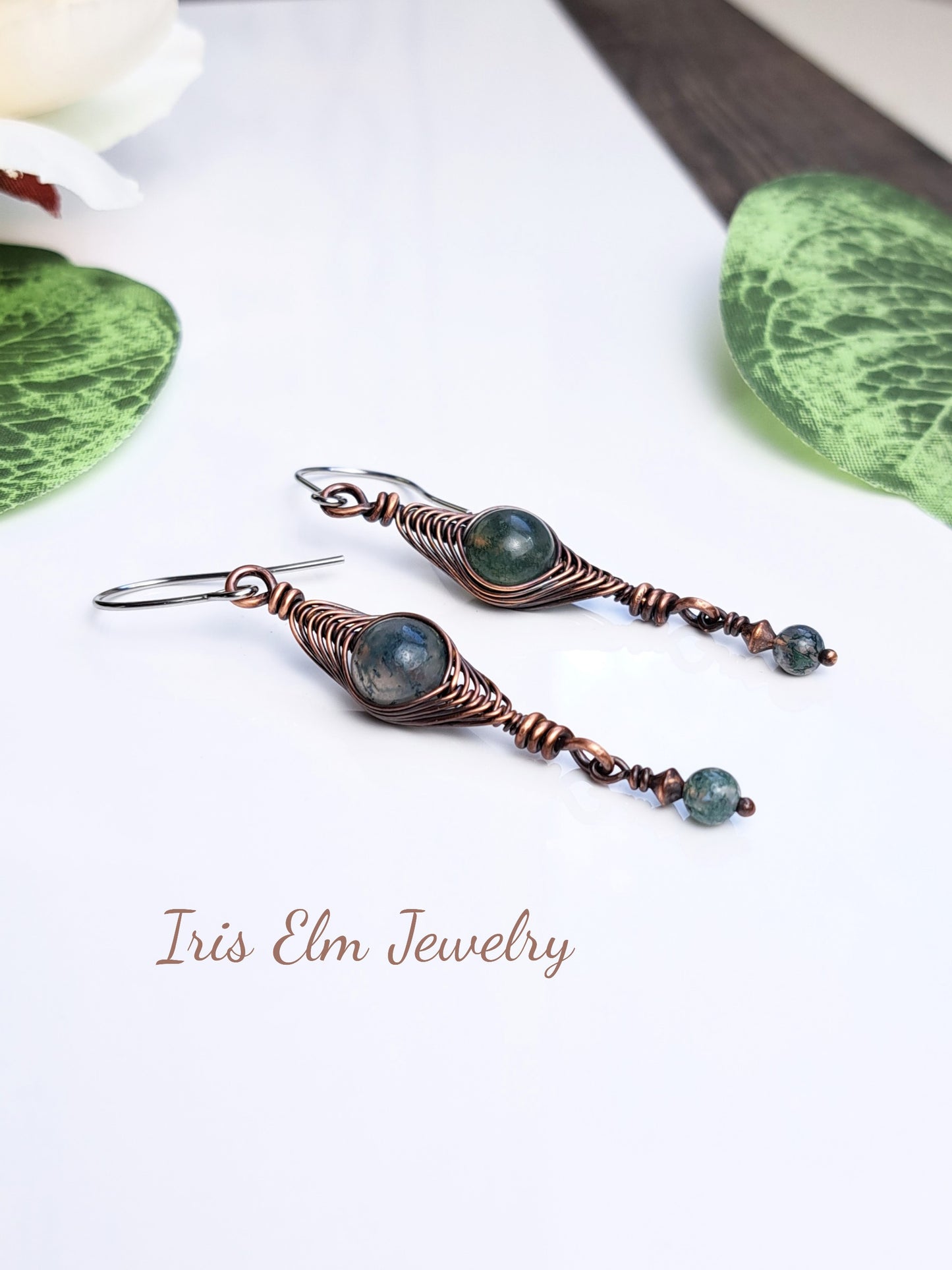 Copper wire-wrapped earrings with green moss agate stone beads on a white background with 'Iris Elm Jewelry' branding.
