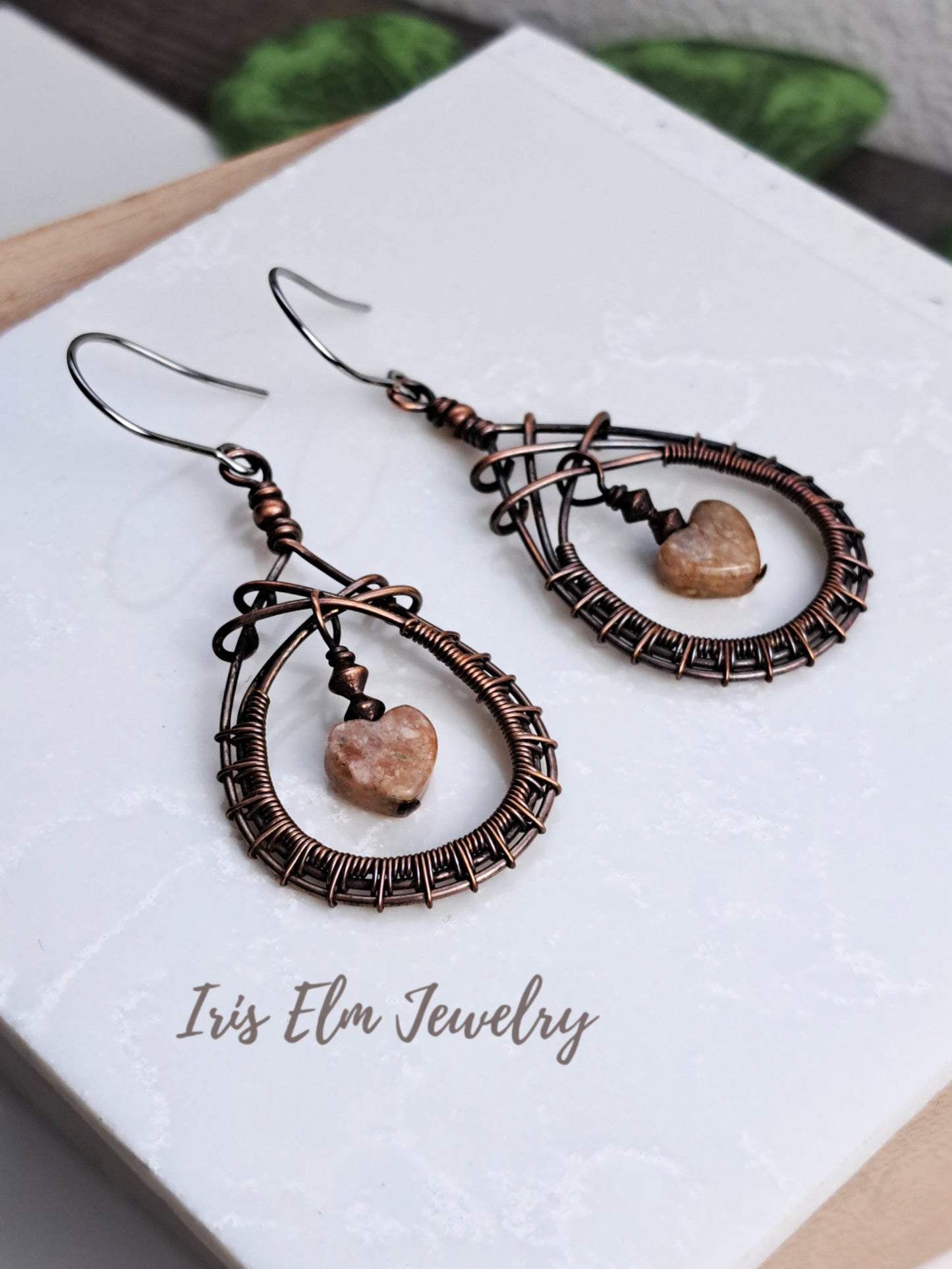 Pair of copper wire-wrapped earrings with heart-shaped stones on a white card with 'Iris Elm Jewelry' branding.
