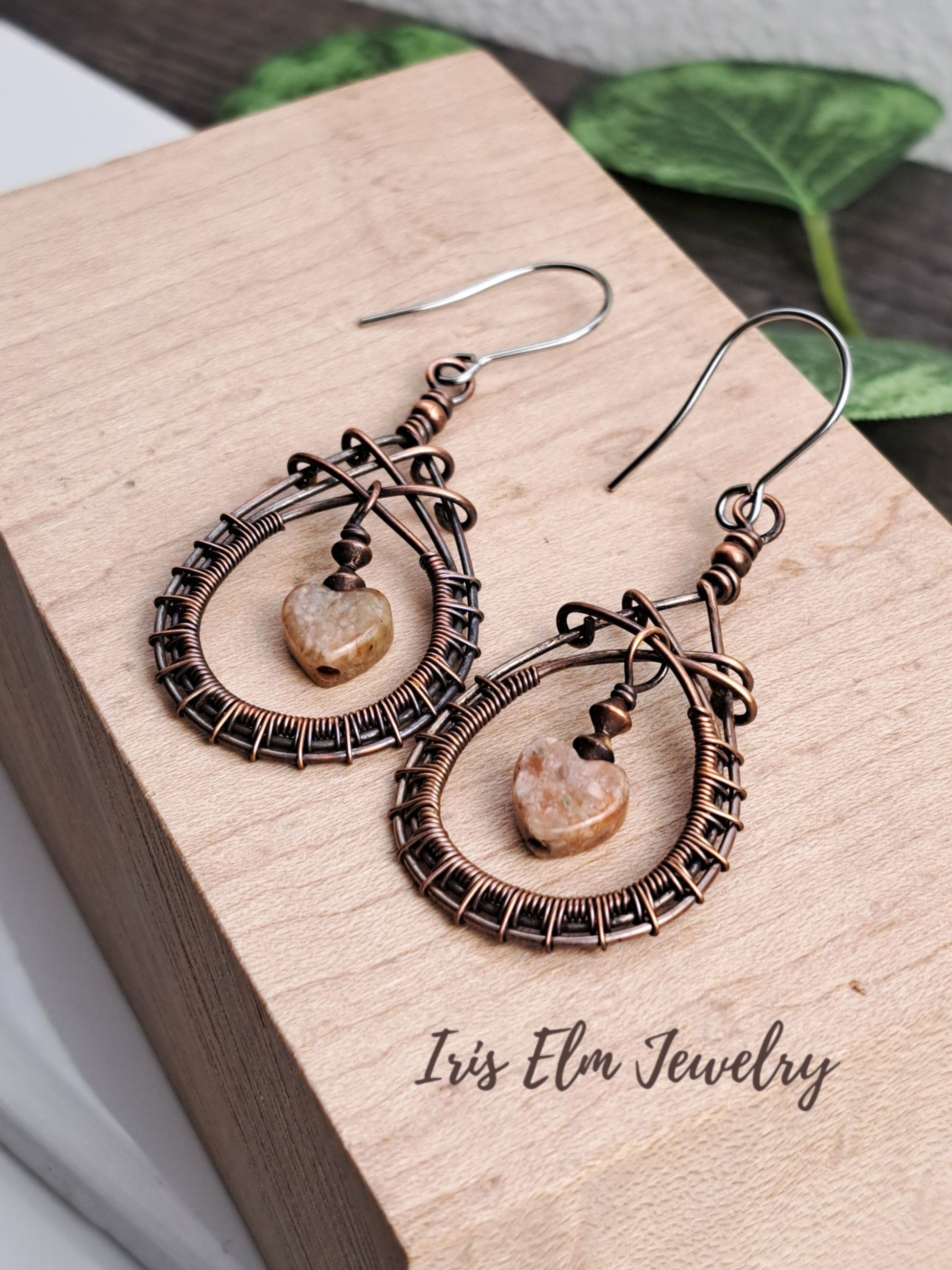 Pair of copper wire-wrapped teardrop earrings with natural stone centers on a wooden surface with 'Iris Elm Jewelry' branding.
