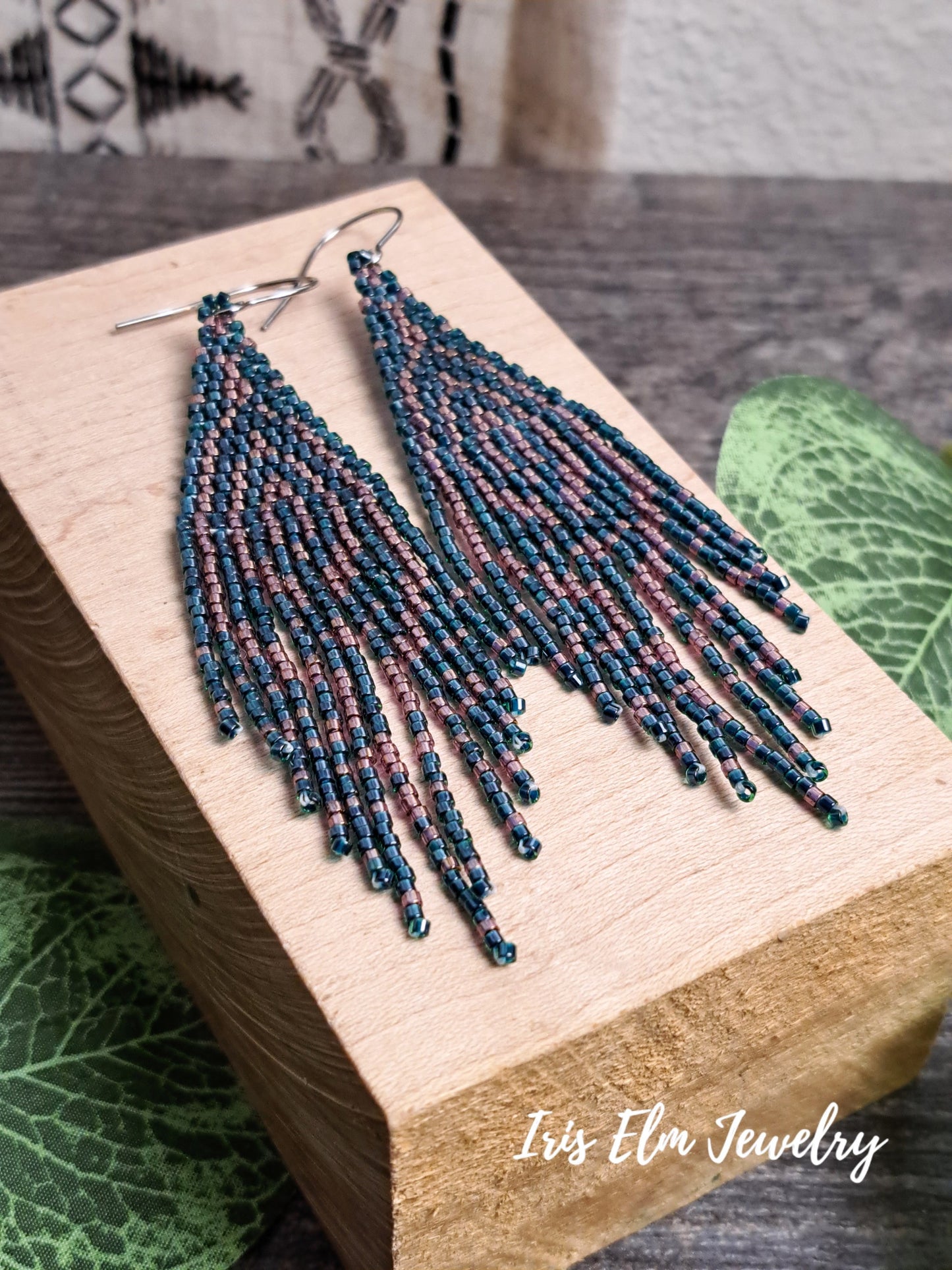 Beadwork handmade forest green and pink seed bead fringe art deco earrings on a wooden block with 'Iris Elm Jewelry' branding.