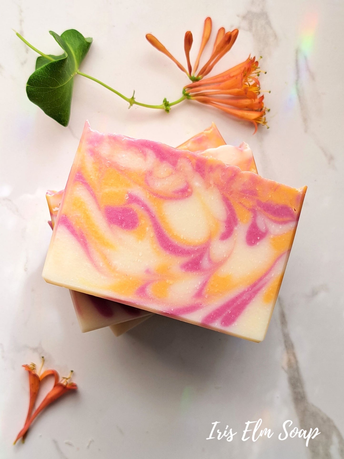 Colorful swirled honeysuckle handmade soap bars on a marble surface with flowers and leaves.