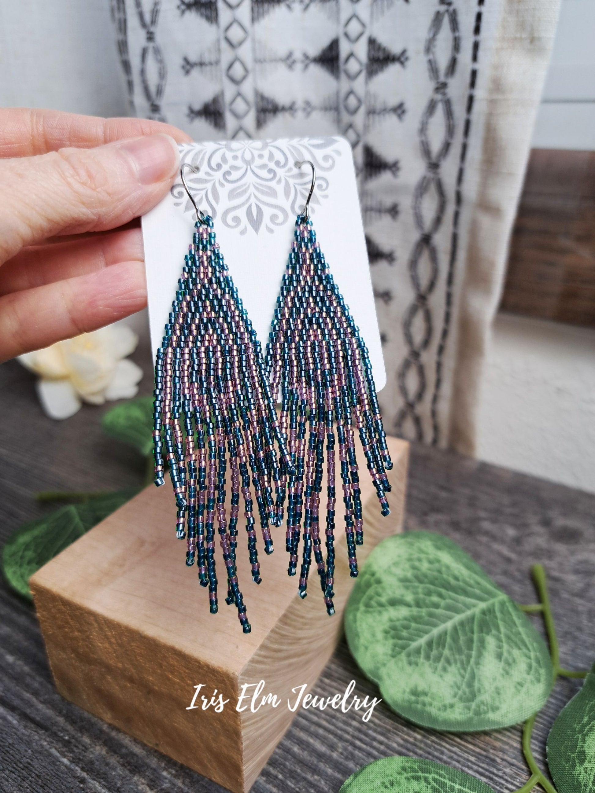 Beaded forest green and pink seed bead fringe art deco glass earrings on a display card held by a hand, with a blurred background