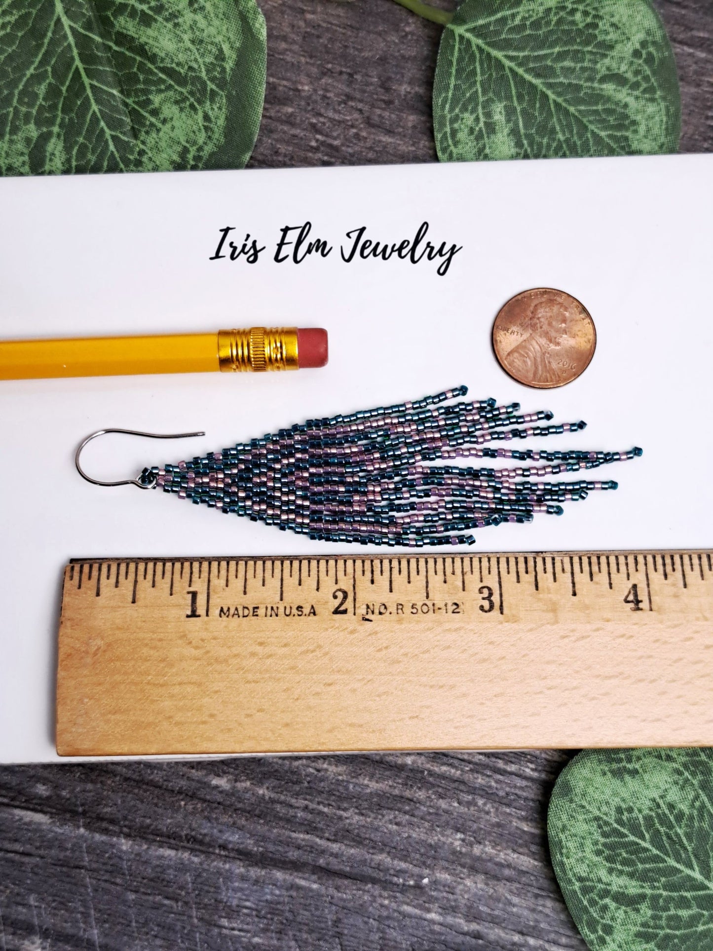 4 inch long Beaded earrings with a ruler for scale, pencil, and coin on a wooden surface with 'Iris Elm Jewelry' branding.