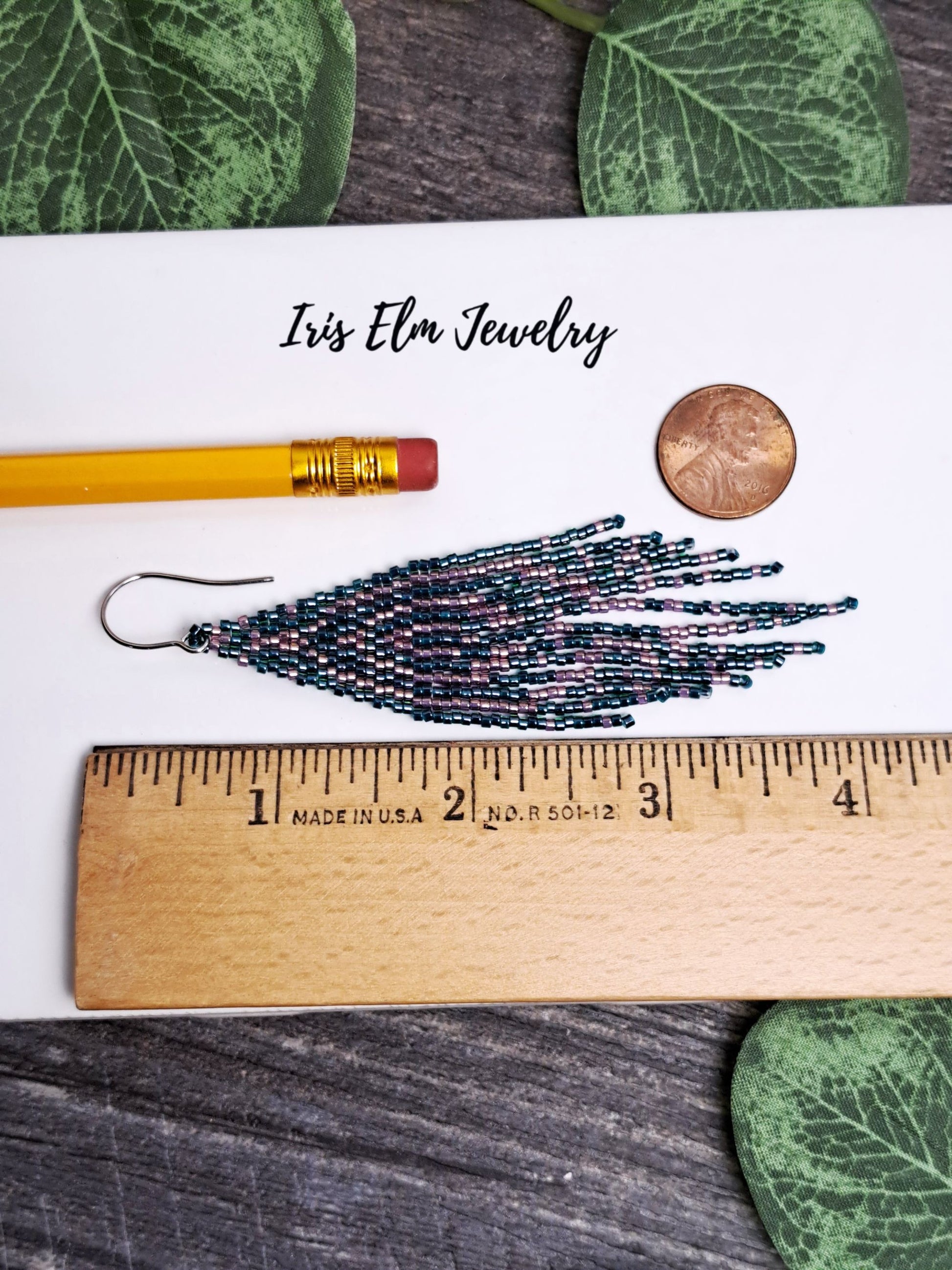 4 inch long Beaded earrings with a ruler for scale, pencil, and coin on a wooden surface with 'Iris Elm Jewelry' branding.