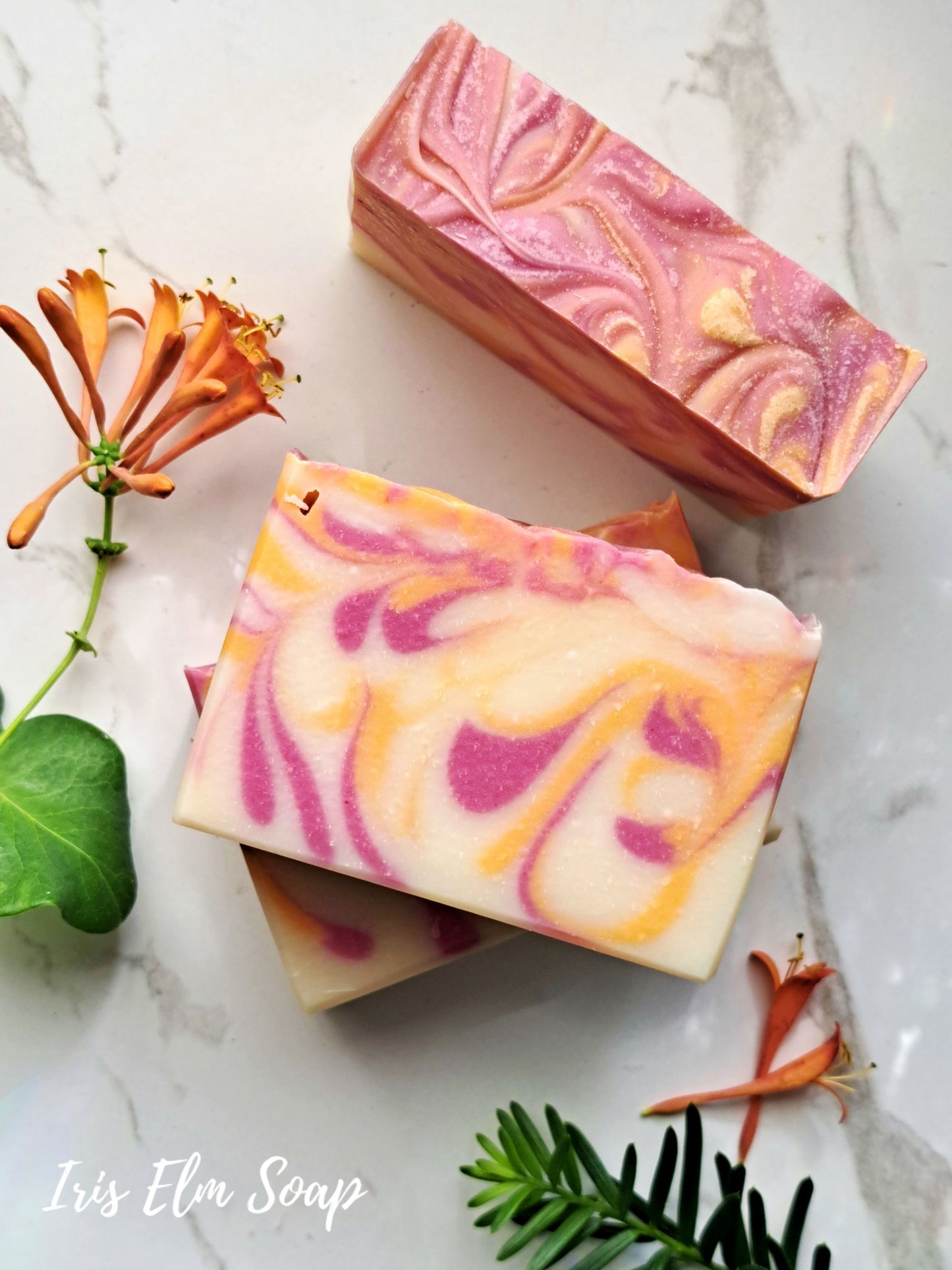 Three swirled honeysuckle handmade soap bars on a marble surface with floral elements.