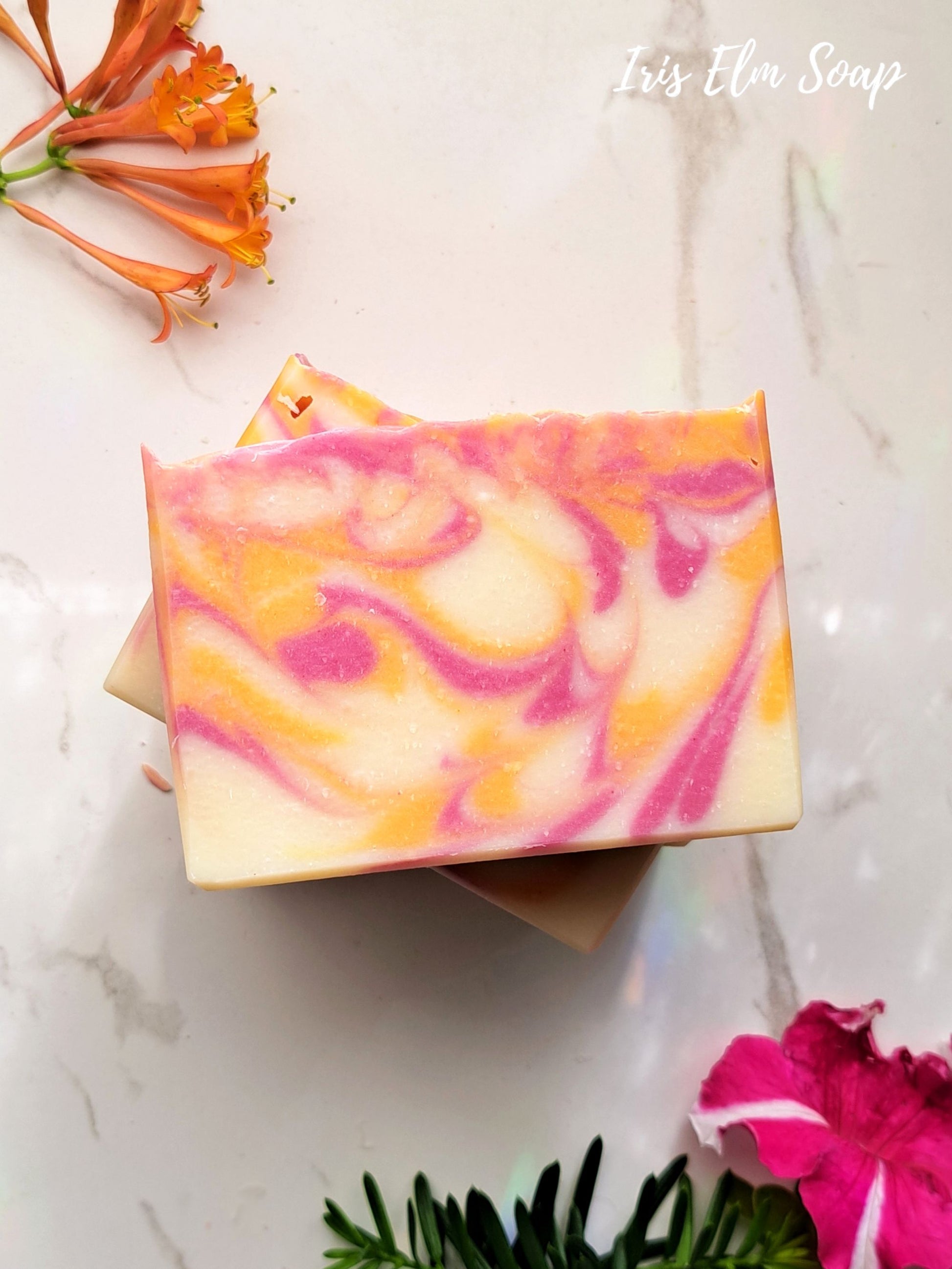 Colorful honeysuckle handmade soap bar with pink and orange swirls on a marble surface, featuring 'Iris Elm Soap' branding.