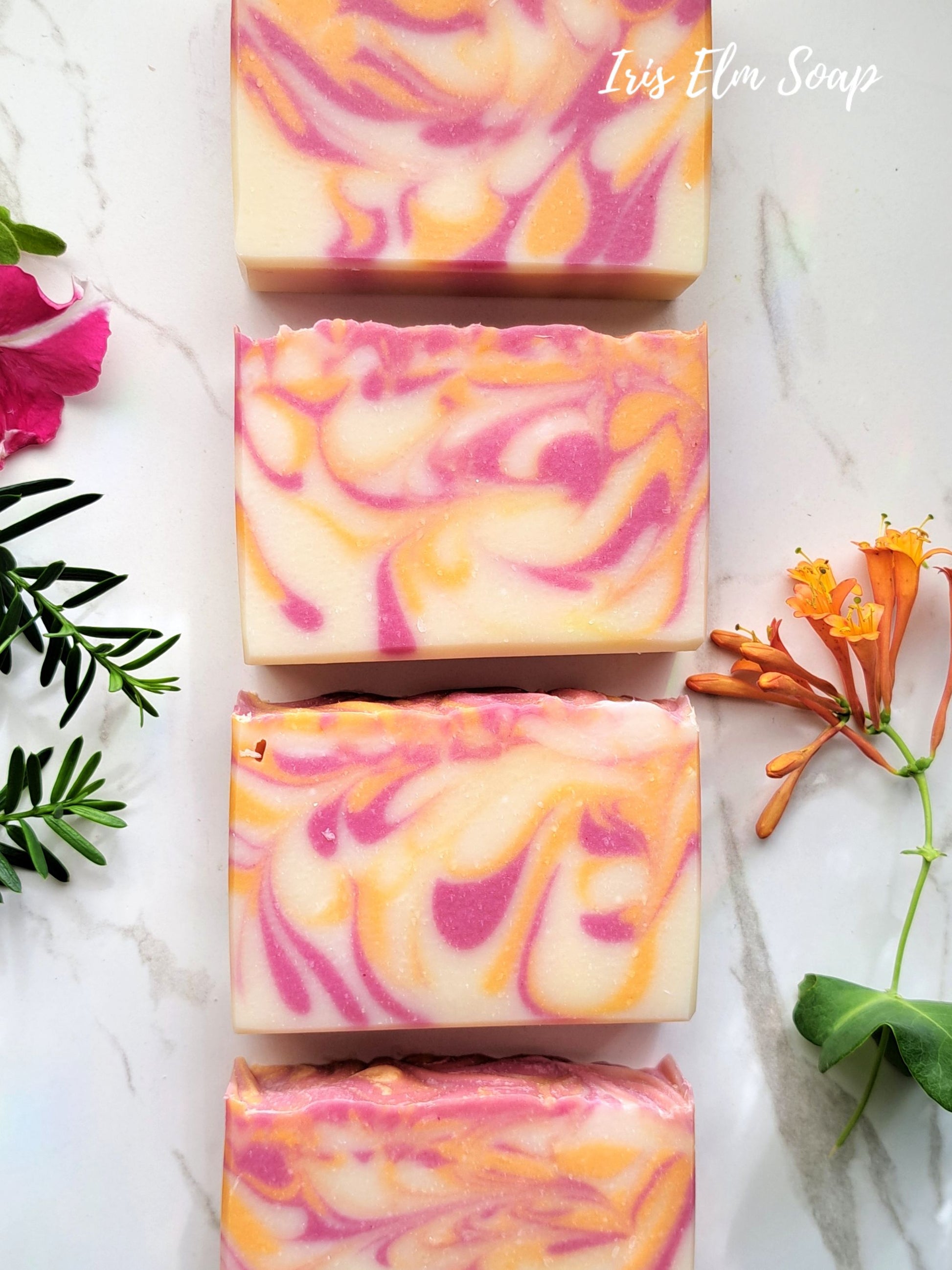 Swirled pink and orange honeysuckle handmade soap bars on a marble surface with floral decorations.