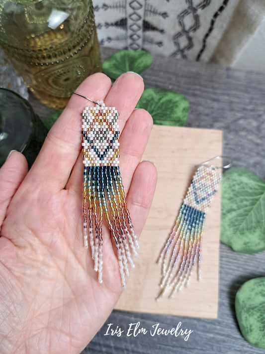 Beaded plaid rainbow seed bead fringe earrings held in a hand with 'Iris Elm Jewelry' branding.