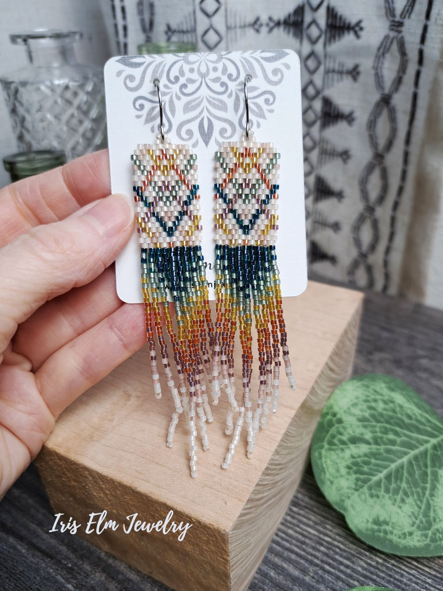Beaded plaid rainbow seed bead fringe earrings on a card held by a hand with 'Iris Elm Jewelry' branding.