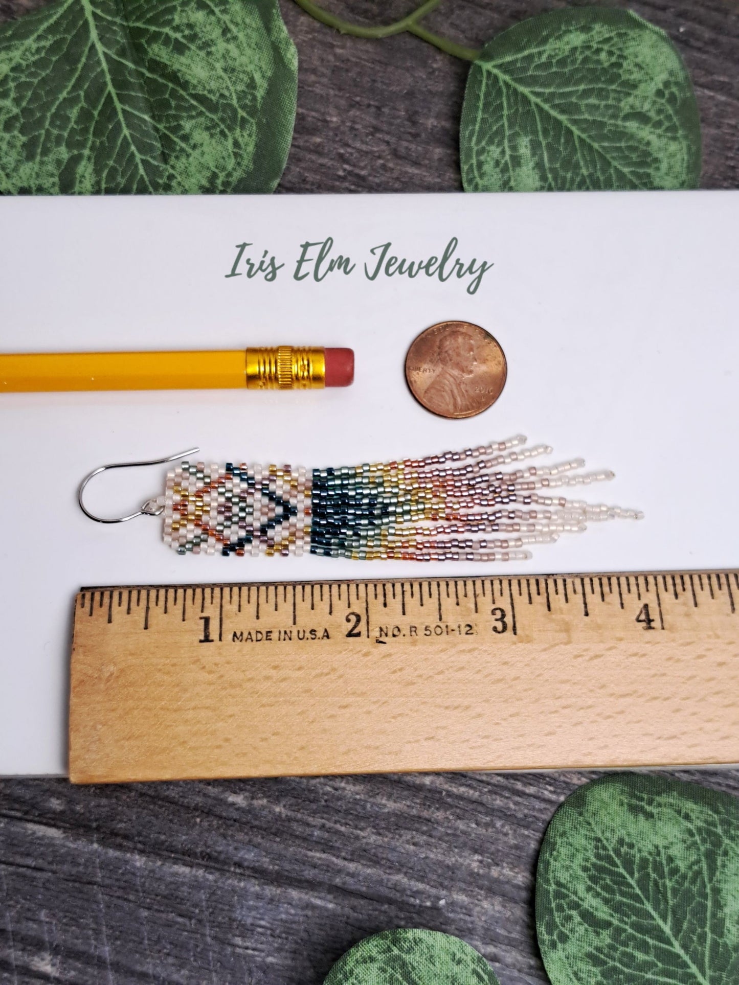 4 inch long Beaded earring on a ruler with 'Iris Elm Jewelry' branding, surrounded by green leaves.