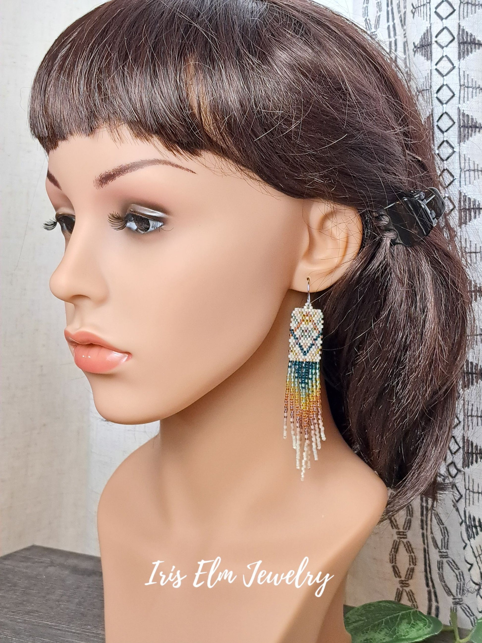 Mannequin head with dark hair styled in a ponytail, wearing colorful beaded earrings with 'Iris Elm Jewelry' branding.