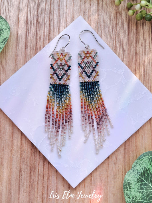 Colorful beaded plaid rainbow seed bead fringe earrings on a white tile with 'Iris Elm Jewelry' branding.