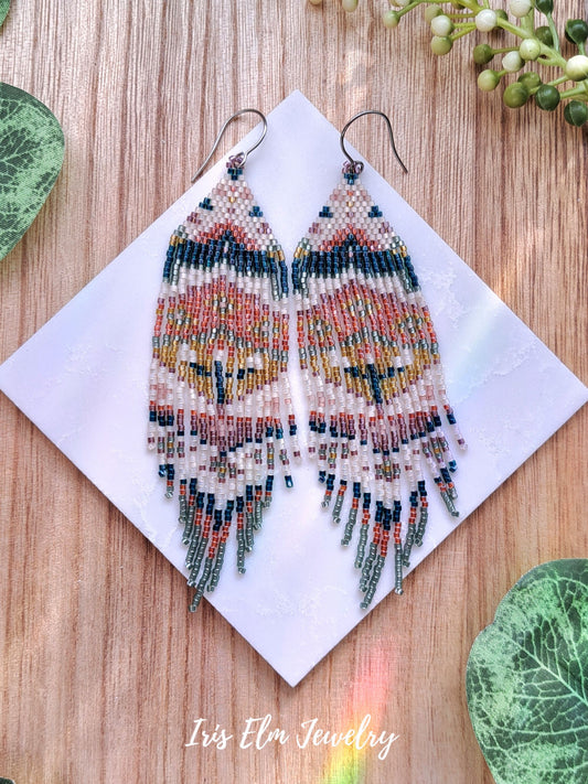 Colorful beaded spring floral folk art seed bead fringe earrings on a wooden surface with 'Iris Elm Jewelry' branding.