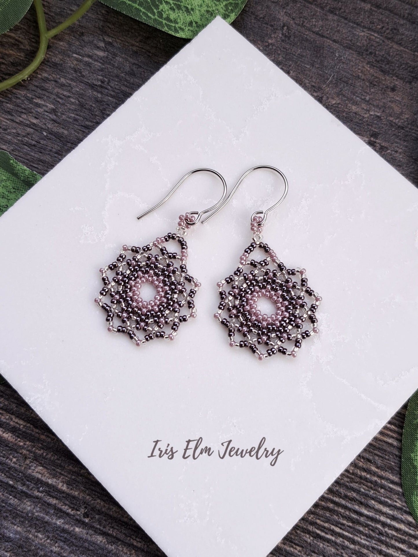 Decorative lilac purple seed bead mandala earrings on a white card with 'Iris Elm Jewelry' branding, placed on a wooden surface.