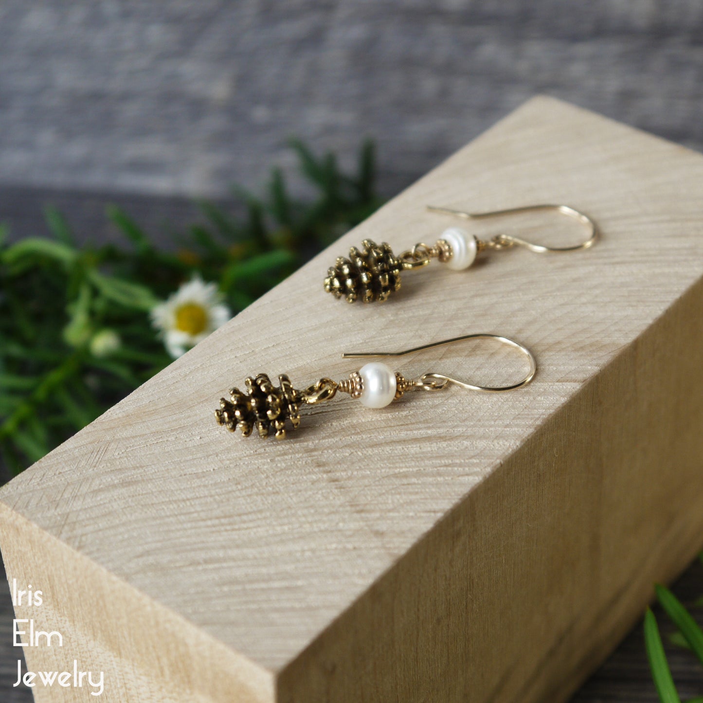 Pair of gold pinecone and pearl handmade earrings on a wooden block with a natural background
