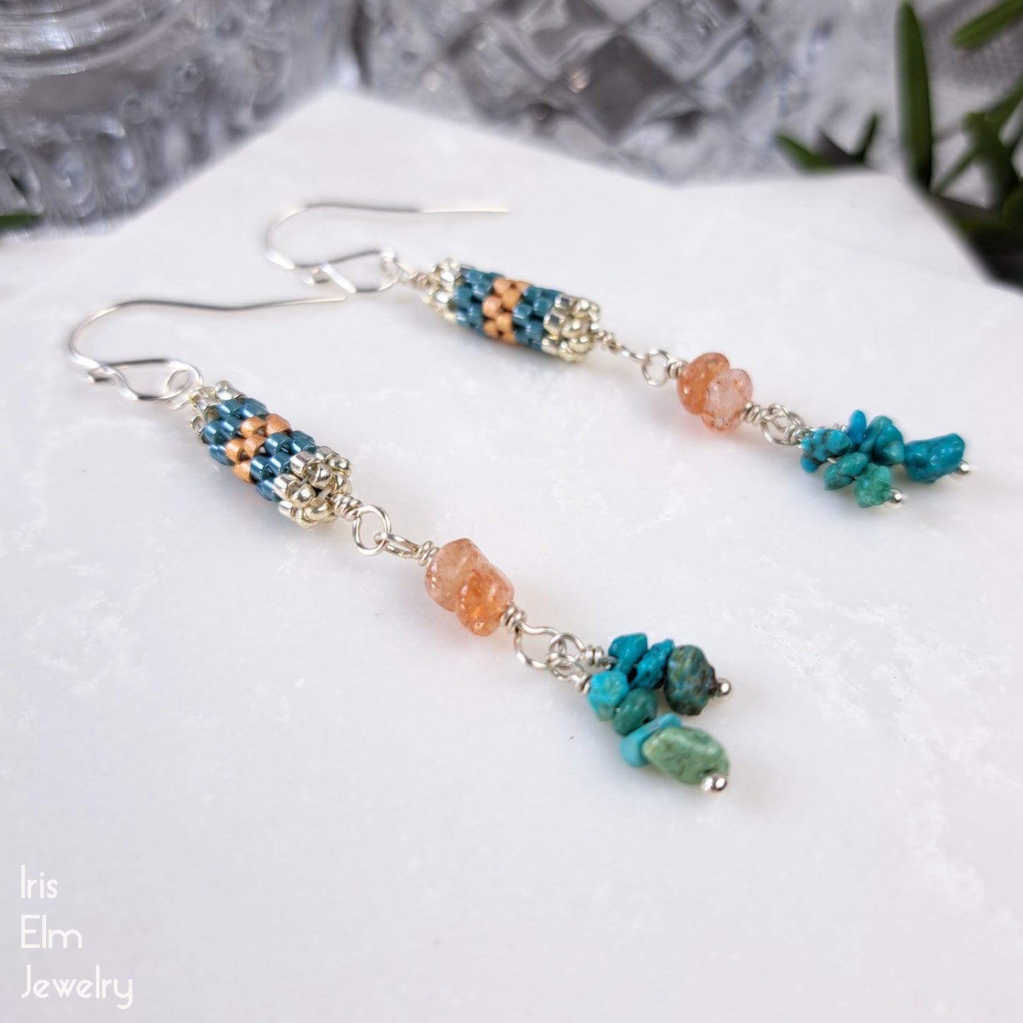 Beaded earrings with turquoise gemstone chips and peach sunstones on a white surface