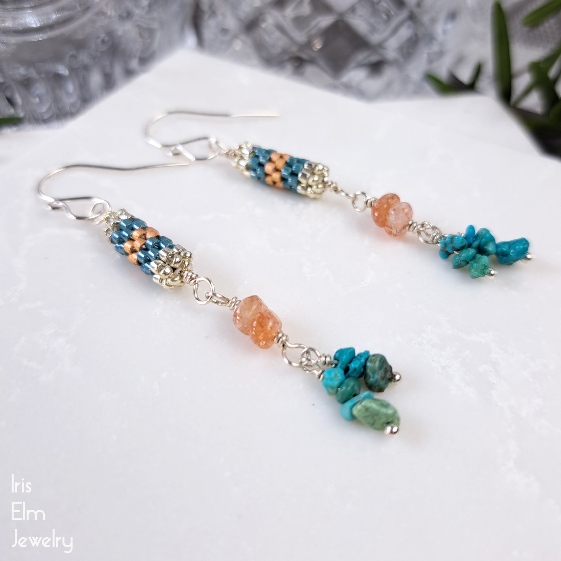 Beaded earrings with turquoise gemstone chips and peach sunstones on a white surface