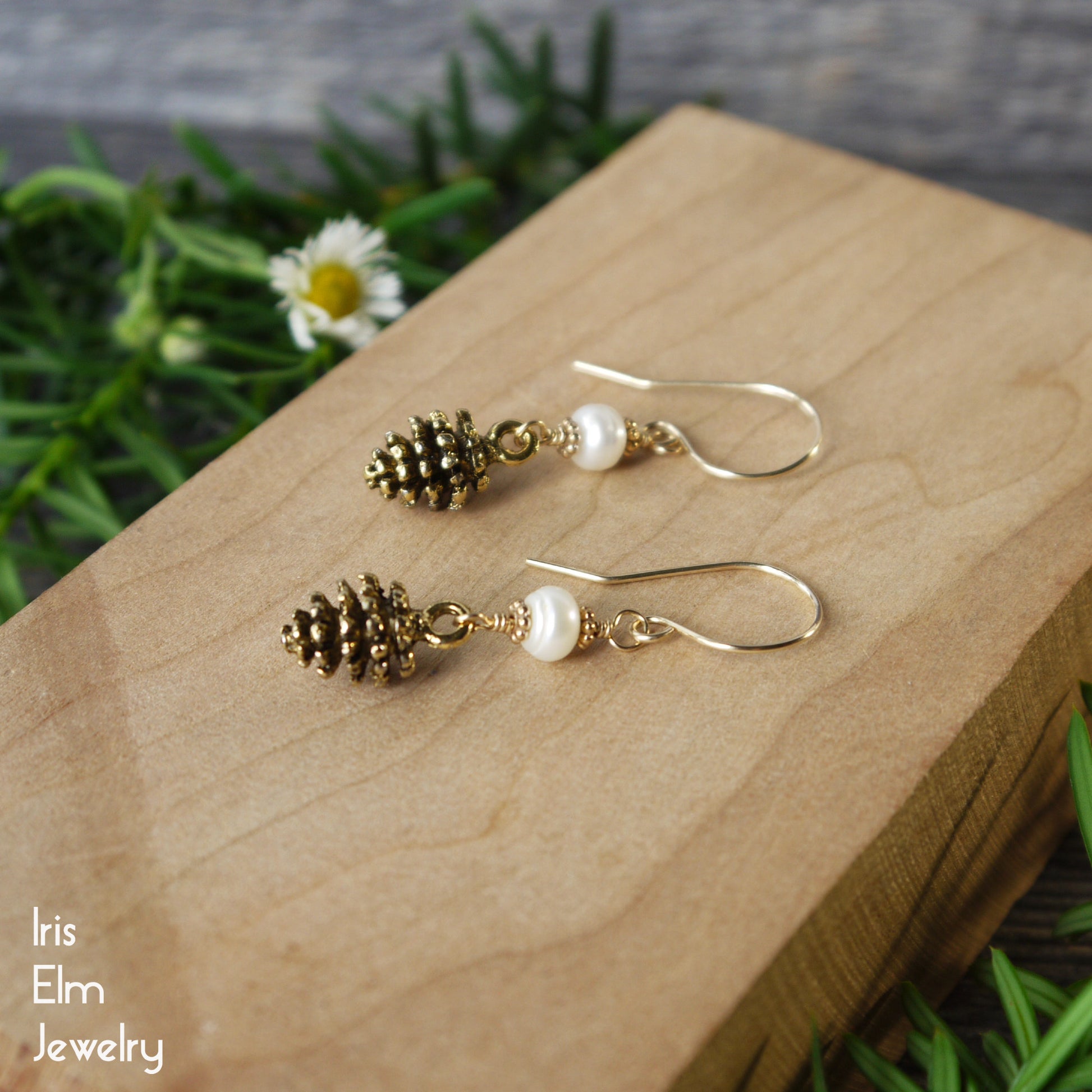 Gold pinecone and pearl earrings on a wooden block with greenery in the background