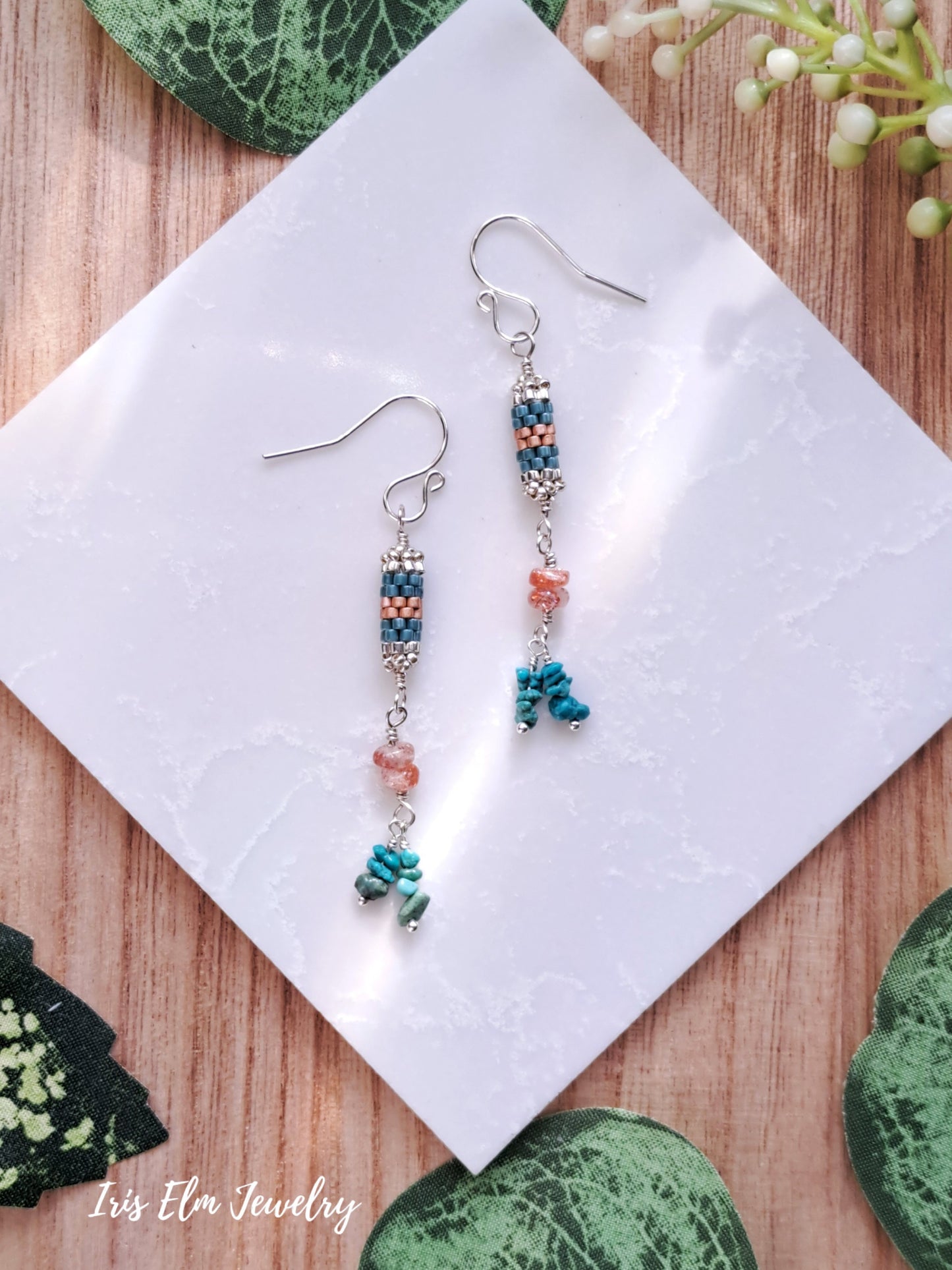 Pair of beaded sunstone and turquoise stone and seed bead sterling silver earrings on a white cloth with 'Iris Elm Jewelry' branding.