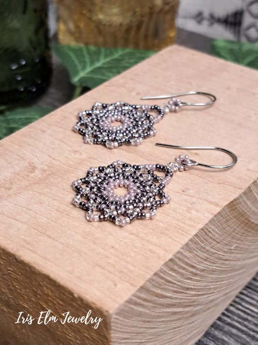 lilac purple beaded mandala seed bead woven earrings on a wooden block with 'Iris Elm Jewelry' branding.