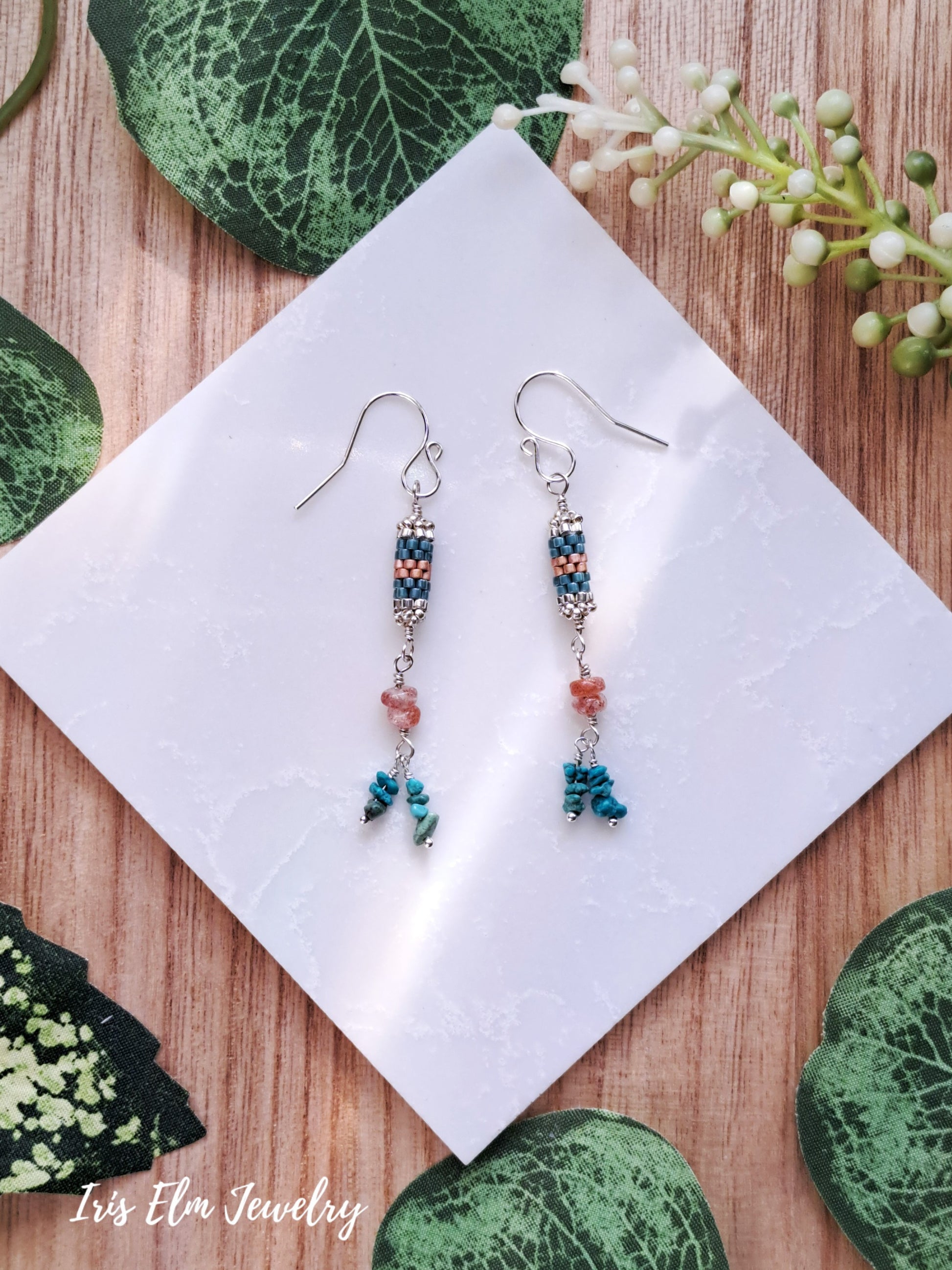 Pair of beaded turquoise and sunstone handmade sterling silver earrings on a white square with green leafy background