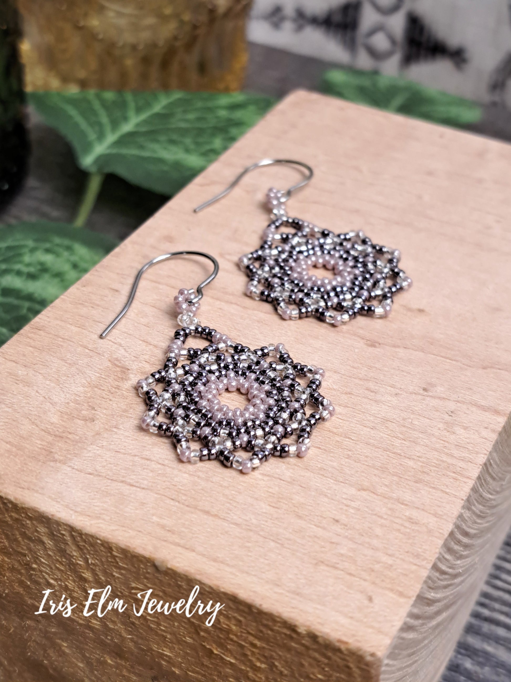 Silver beaded lilac purple seed bead mandala earrings on a wooden block with 'Iris Elm Jewelry' branding.