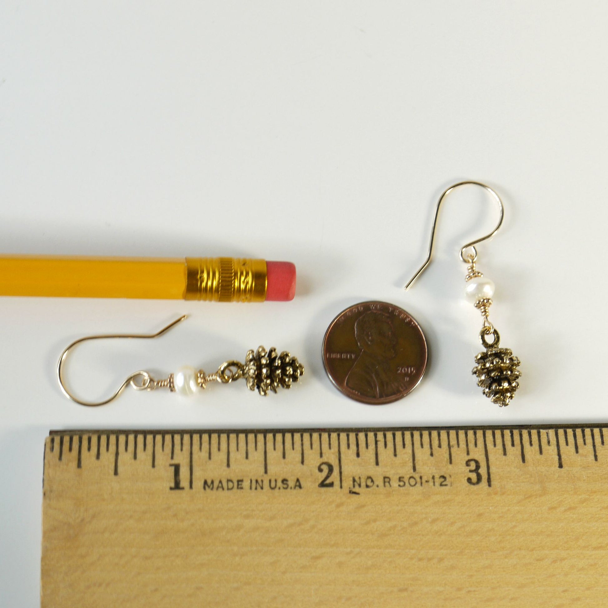 1.75 inch long Gold earrings with pine cone designs and white pearls on a ruler and penny for scale on a white background
