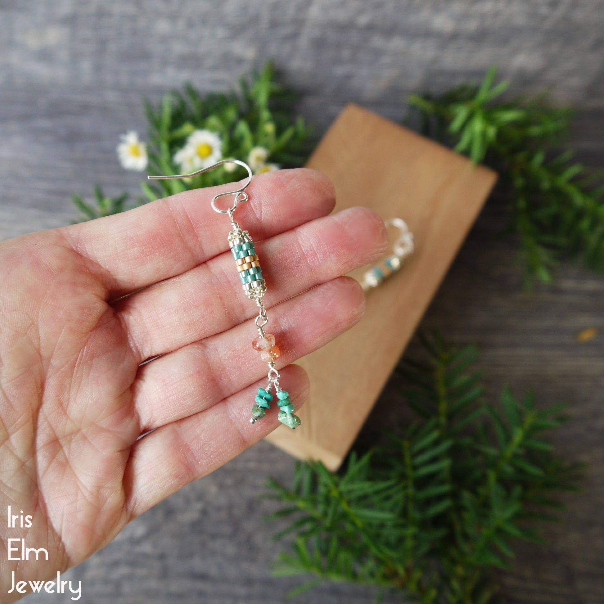 Hand holding a pair of beaded seed bead earrings with sunstone and turquoise gemstone chips dangling with a natural background