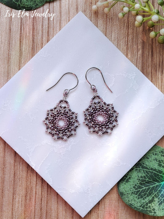 Pair of lilac purple beadwoven seed bead mandala earrings on a white napkin with 'Iris Elm Jewelry' branding.