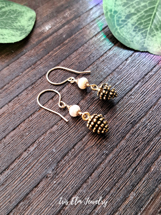 Gold pinecone freshwater pearl earrings on a wooden surface with 'Iris Elm Jewelry' branding.