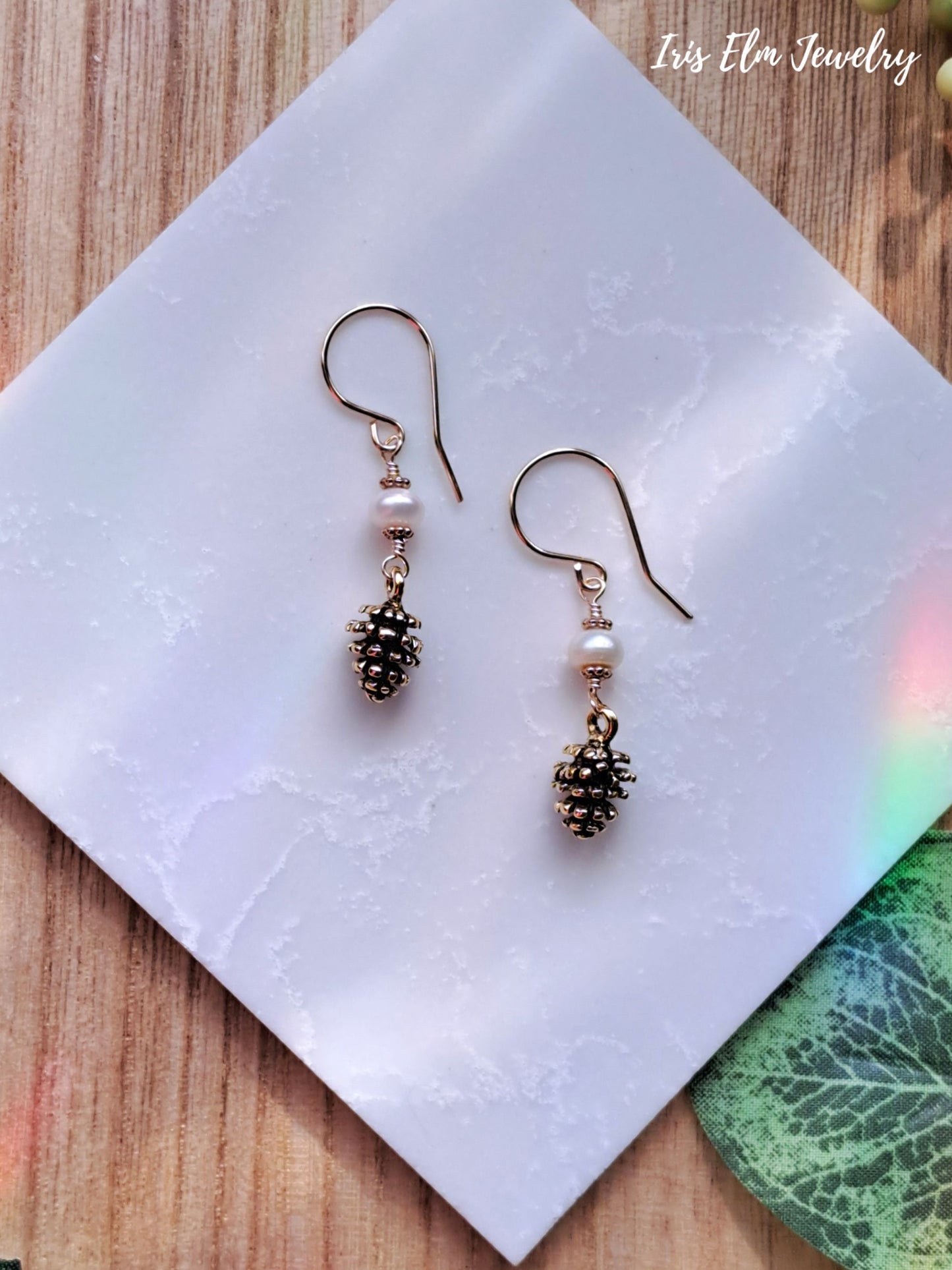 Pair of earrings with pine cone and pearl details on a white napkin.