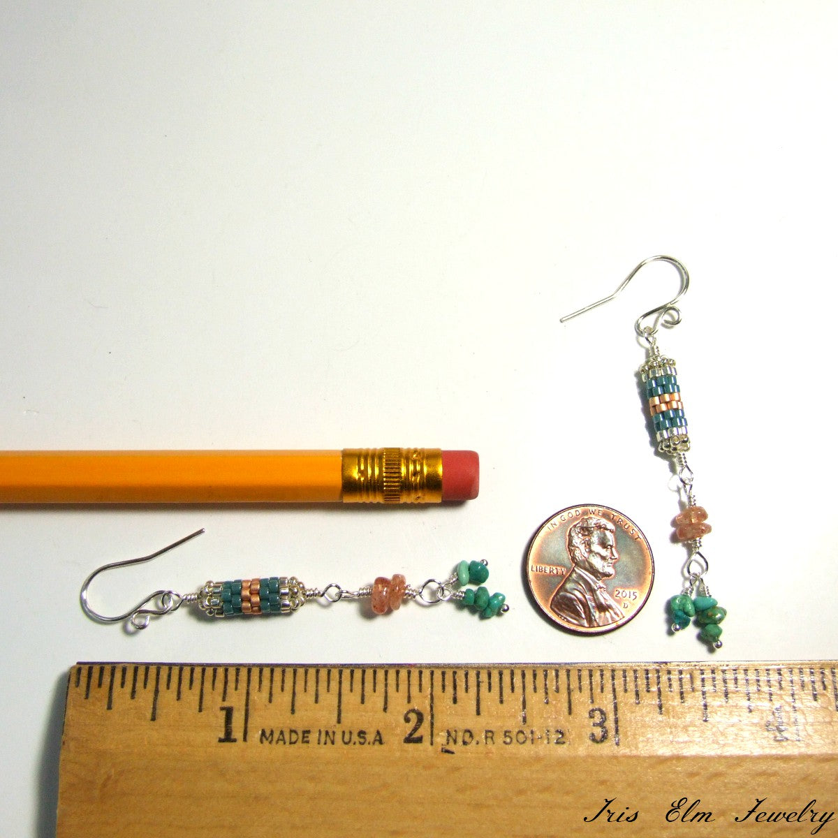 Pair of beaded earrings next to a penny and ruler for scale on a white background