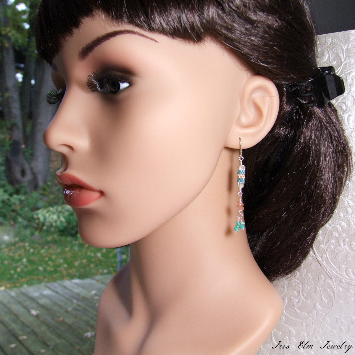 Mannequin head with a turquoise and sunstone dangling earring, set against a blurred natural background