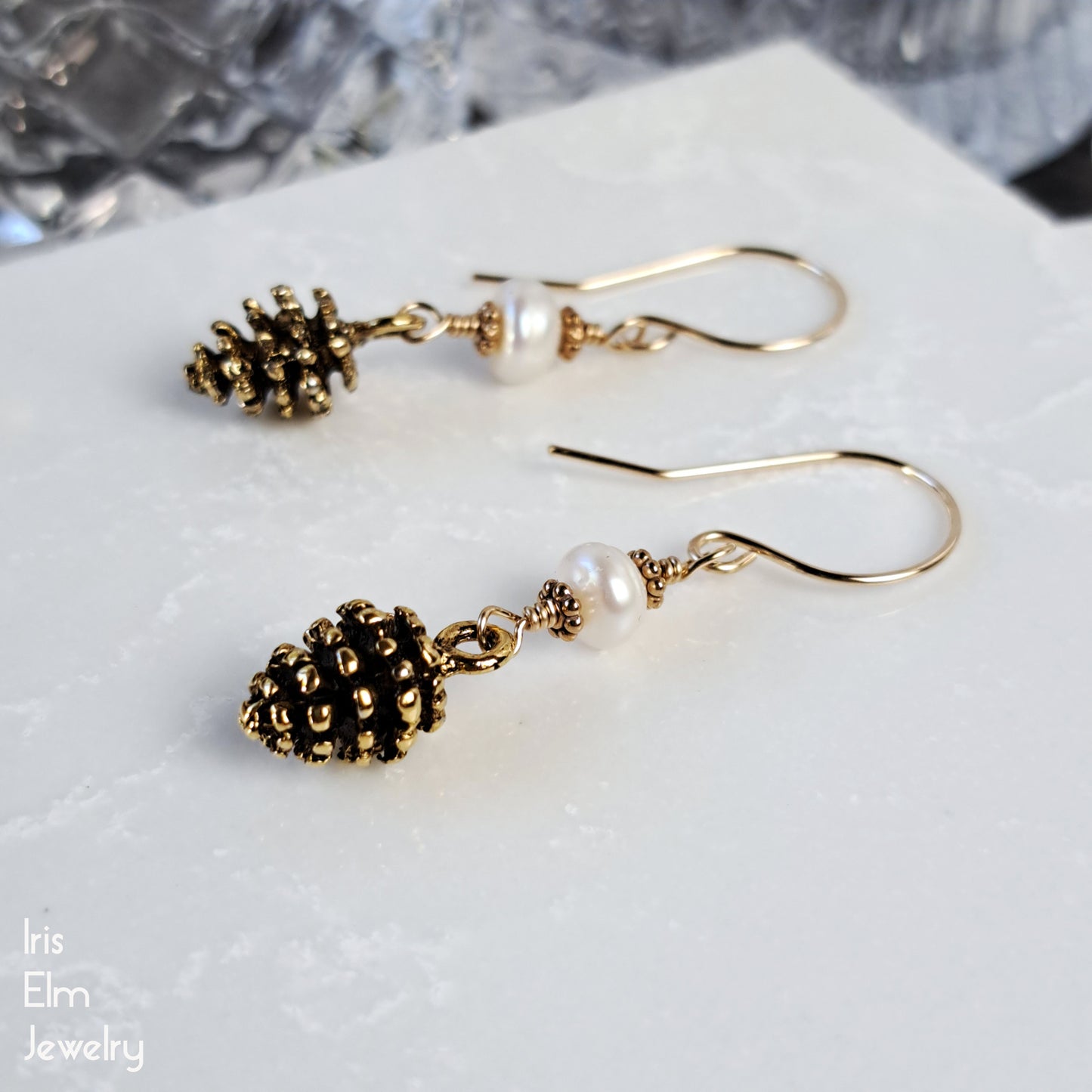 Gold tone pinecone earrings with pearl-like beads on a white surface, branded 'Iris Elm Jewelry'.