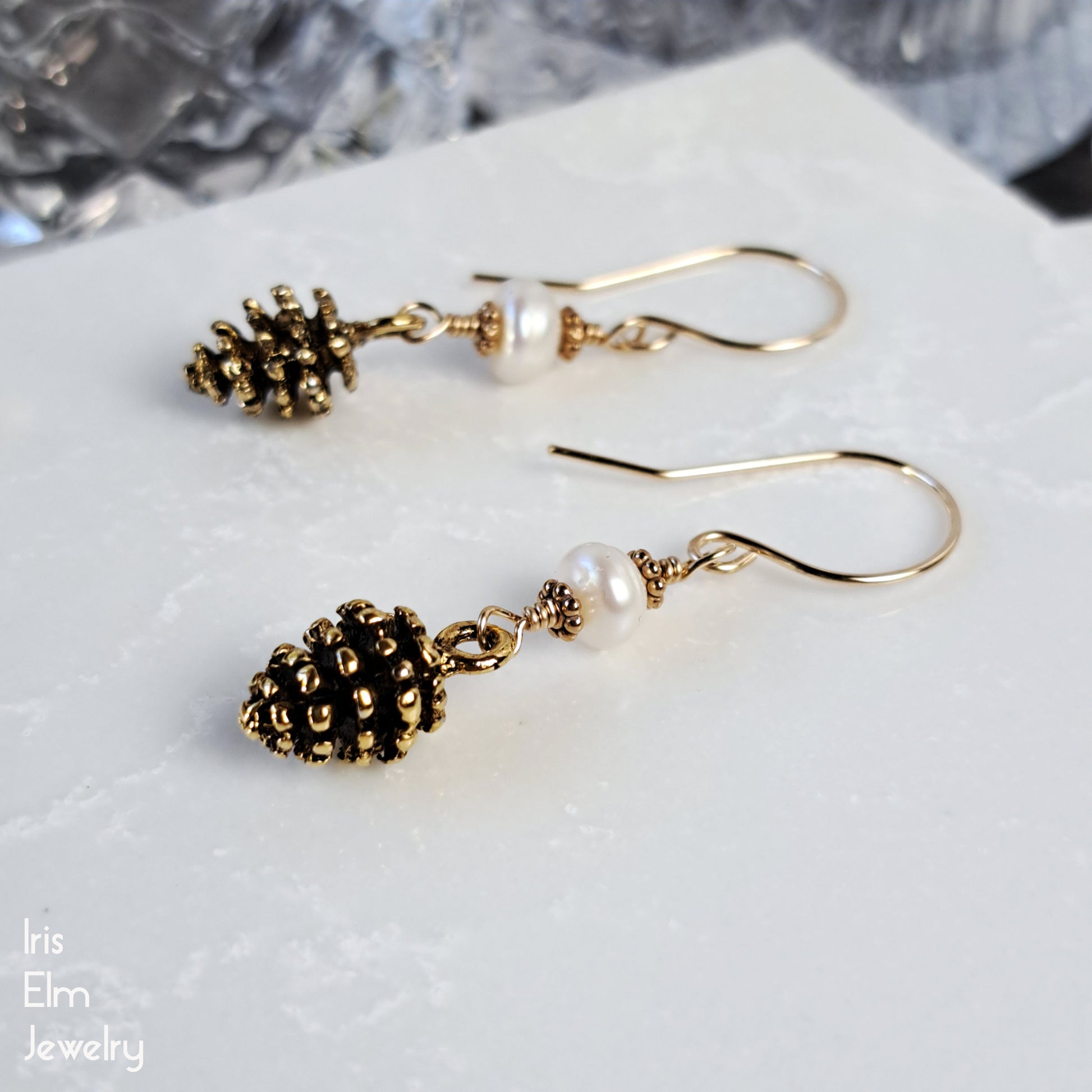 Gold tone pinecone earrings with pearl-like beads on a white surface, branded 'Iris Elm Jewelry'.