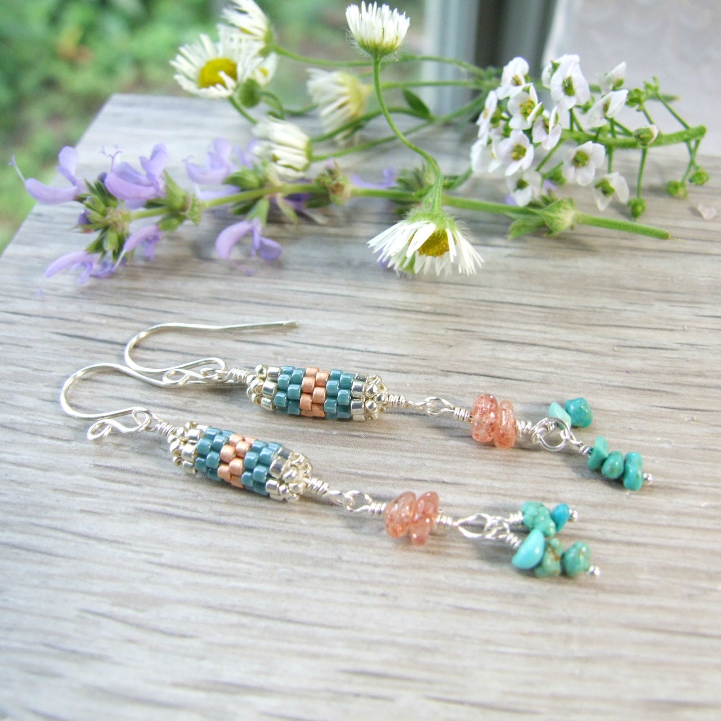 handmade sterling silver Beaded turquoise and sunstone earrings on a wooden surface with flowers in the background