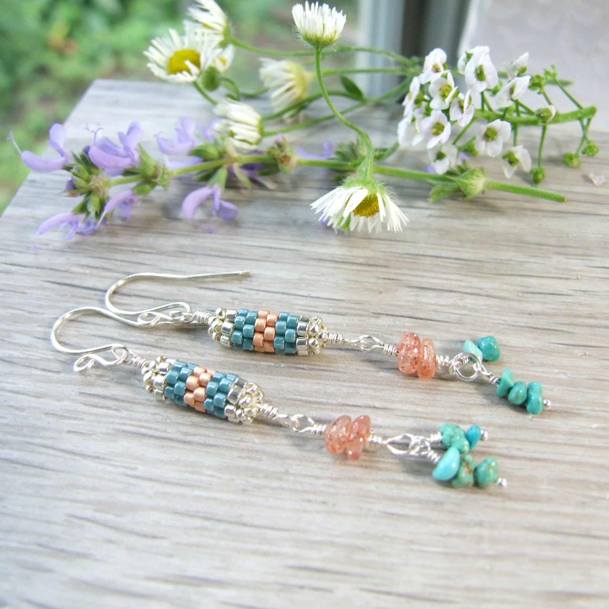 handmade sterling silver Beaded turquoise and sunstone earrings on a wooden surface with flowers in the background