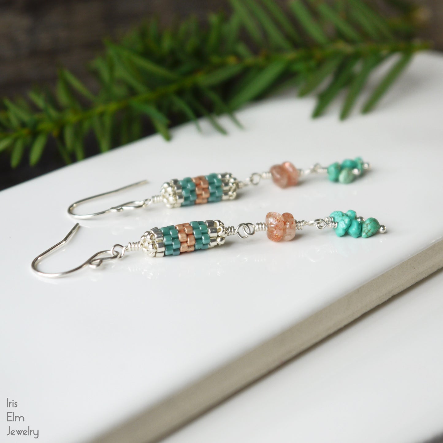 Beaded peach sunstone and turquoise stone earrings on a white surface with greenery in the background