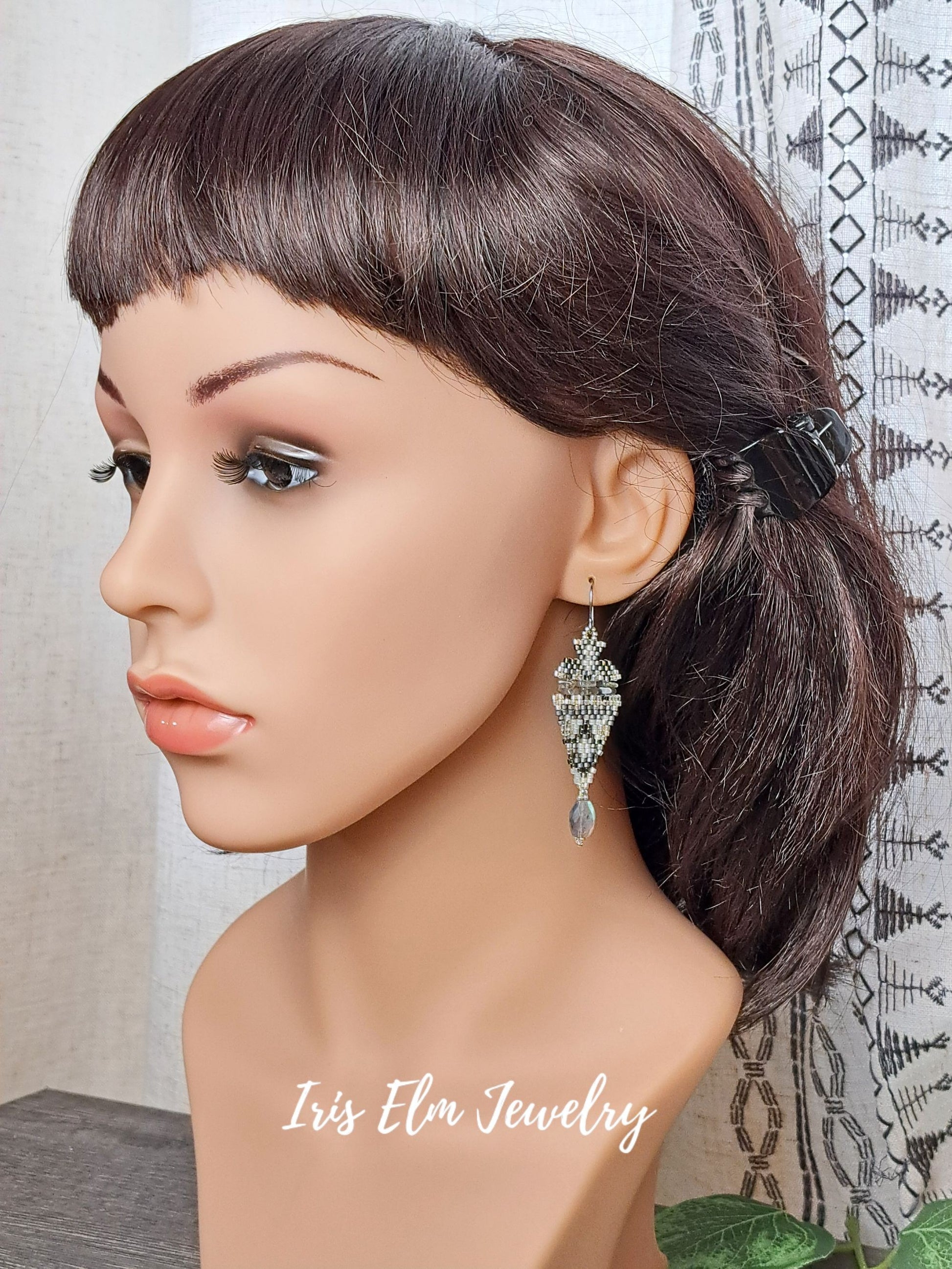 Mannequin head with dark hair styled in a ponytail, wearing iridescent labradorite stone and seed bead boho beadwork earrings with 'Iris Elm Jewelry' branding.
