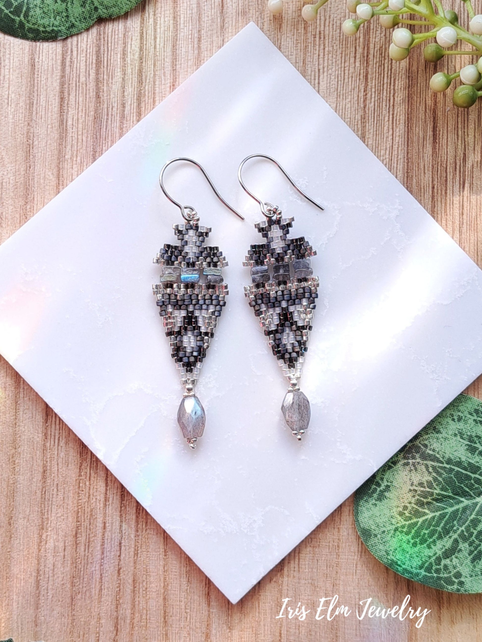Pair of beaded labradorite stone and seed bead earrings on a white square with 'Iris Elm Jewelry' branding, placed on a wooden surface.