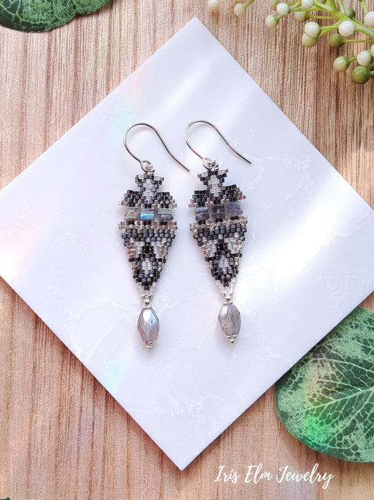 Pair of beaded labradorite stone and seed bead earrings on a white square with 'Iris Elm Jewelry' branding, placed on a wooden surface.