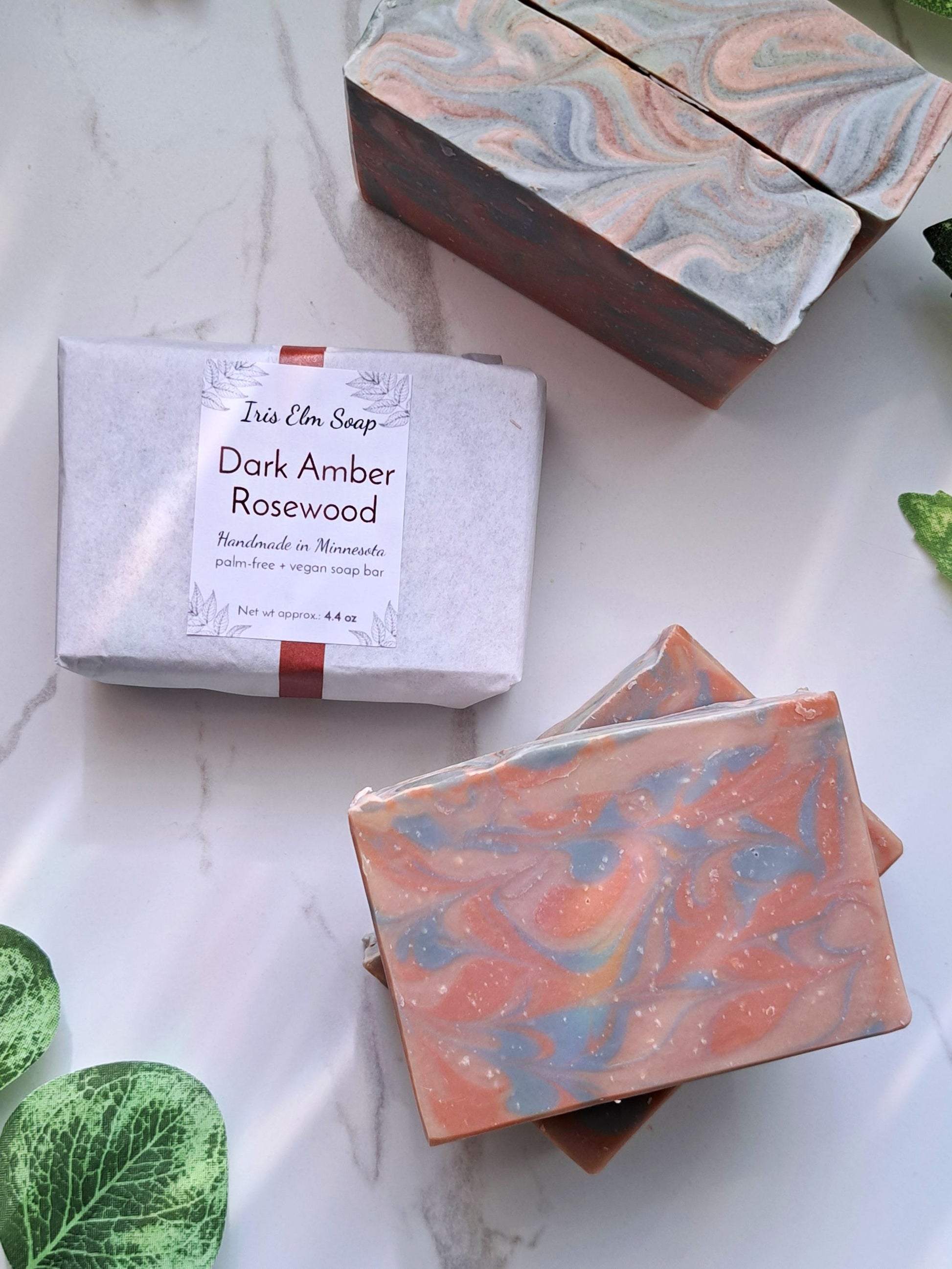 Marbled soap bars and packaging labeled 'Dark Amber Rosewood' on a marble surface.